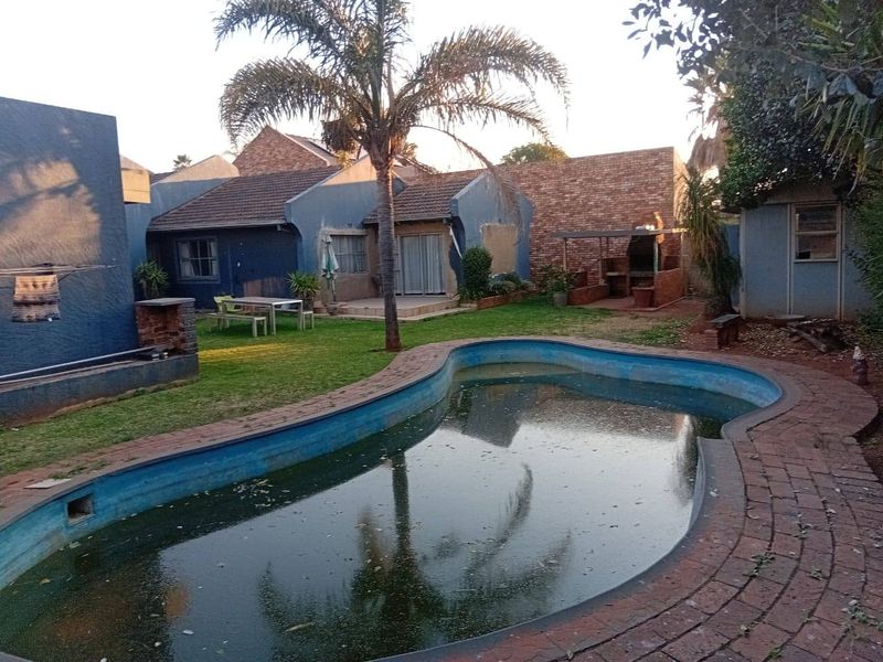 Rear garden area featuring a swimming pool, brick paving, and a built-in braai, set against the rear elevation of the house.