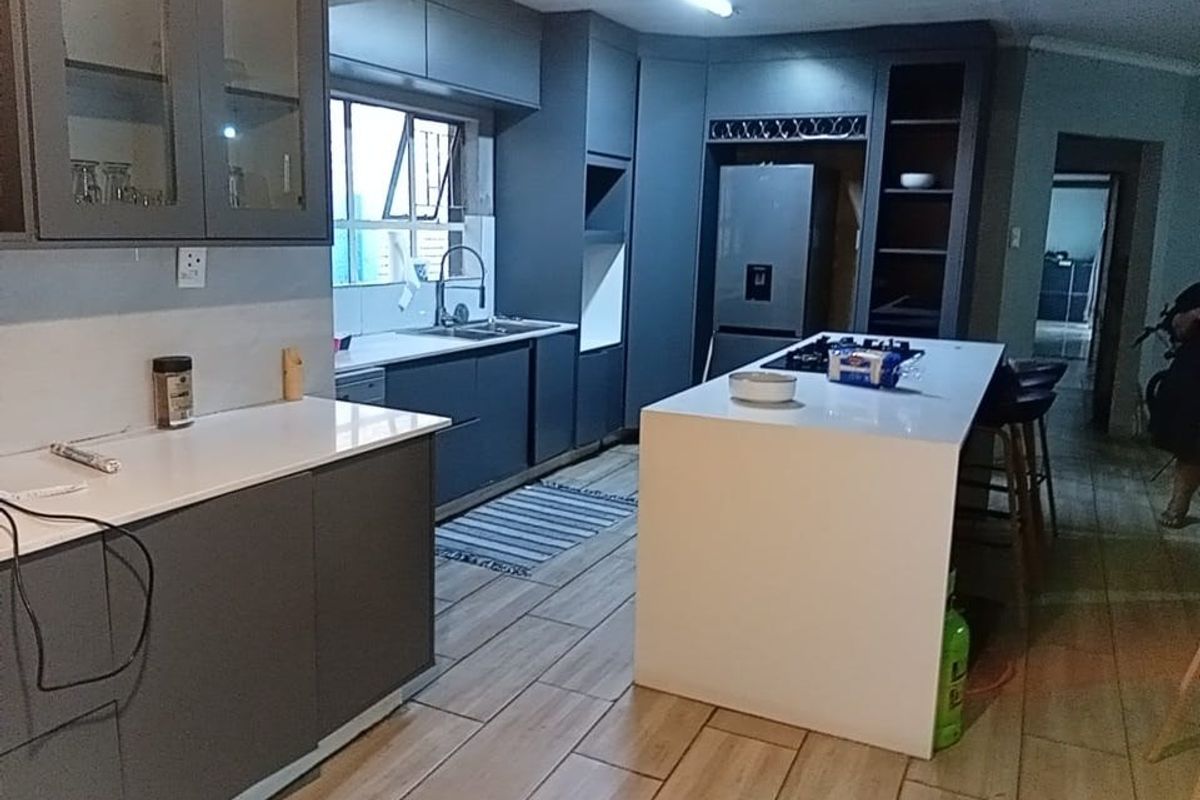 Modern kitchen featuring dark grey cabinetry, a central island with a white countertop, gas hob, and tiled flooring throughout.