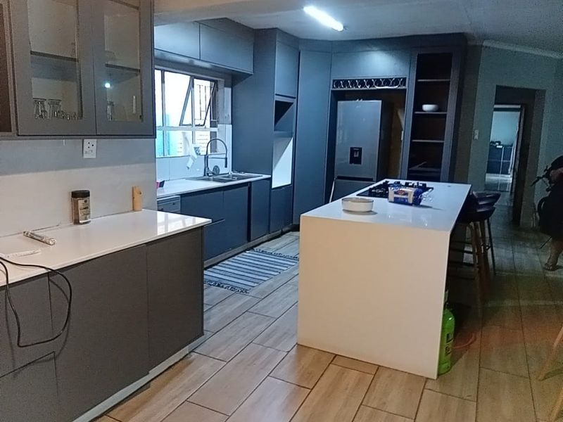 Modern kitchen featuring dark grey cabinetry, a central island with a white countertop, gas hob, and tiled flooring throughout.