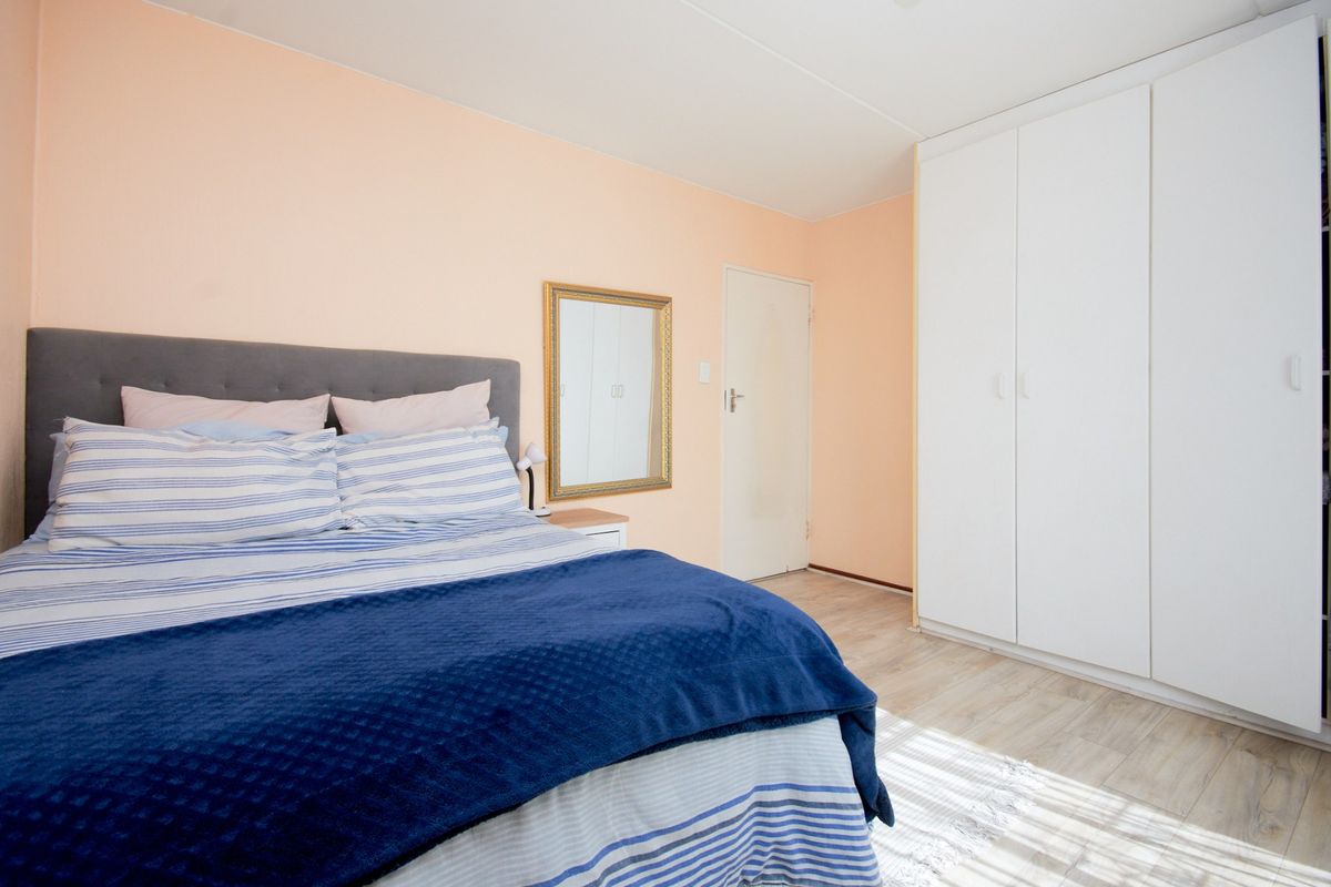 A bedroom featuring light-toned laminate flooring and a large white built-in wardrobe with ample storage space.
