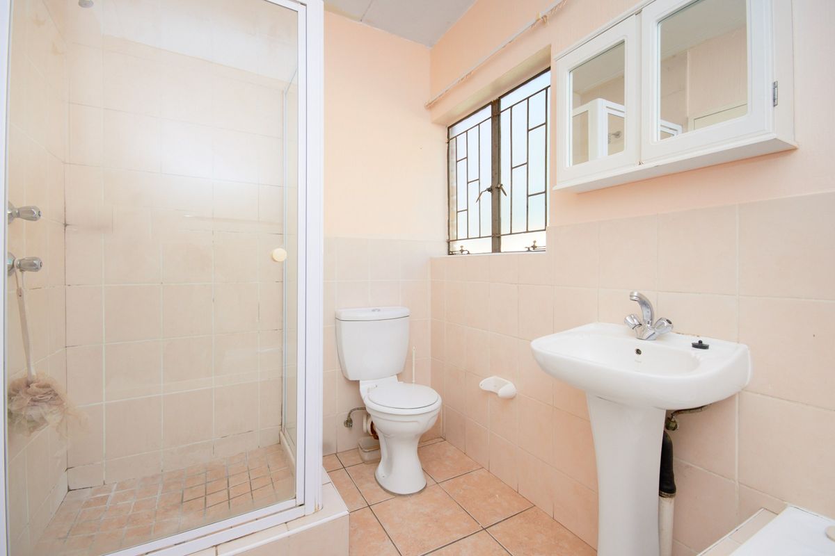 A functional bathroom featuring a shower enclosure, pedestal basin, toilet, and wall-mounted medicine cabinet with neutral tiled finishes.