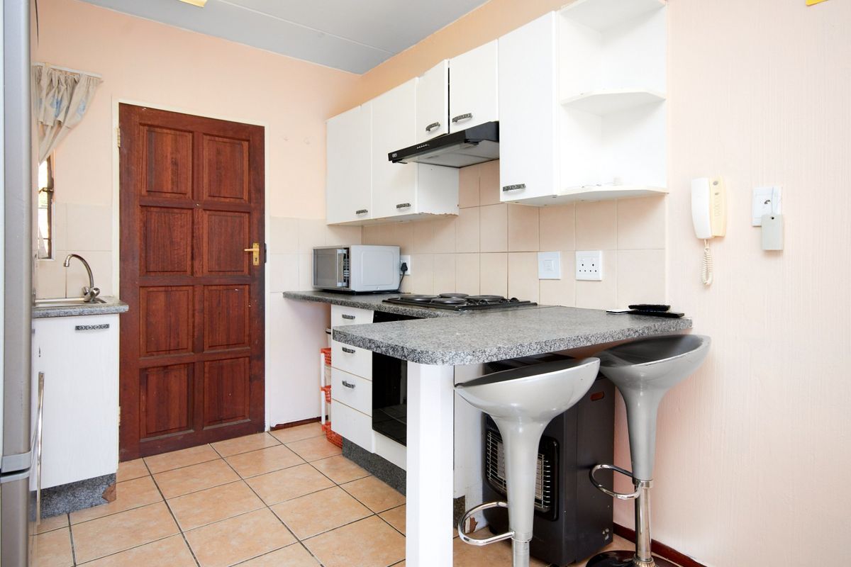 Compact kitchen featuring white cabinetry, granite countertops, integrated hob with extractor fan, and tiled flooring, providing a functional workspace.