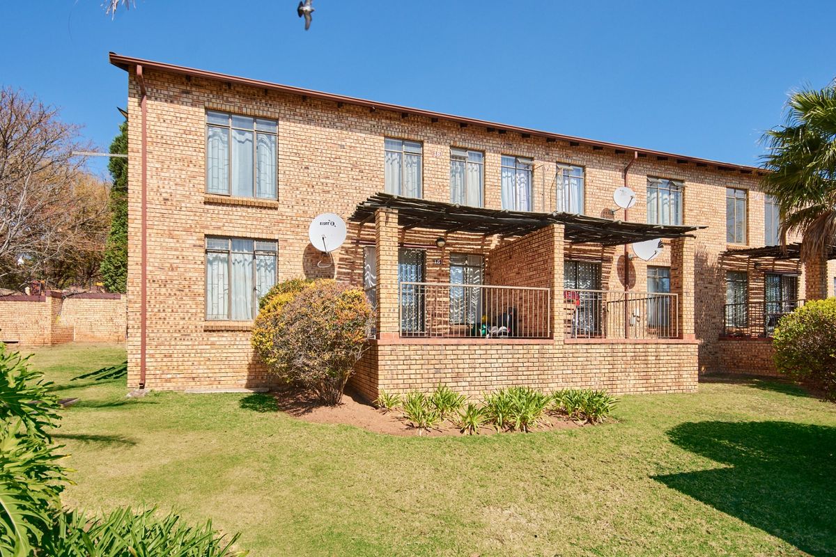 Rear view of a multi-story face brick apartment building featuring ground floor patios with pergolas and established garden space.