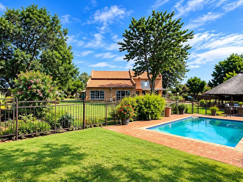 A well-maintained backyard featuring a swimming pool with brick surround, a traditional thatched lapa, and established garden landscaping.