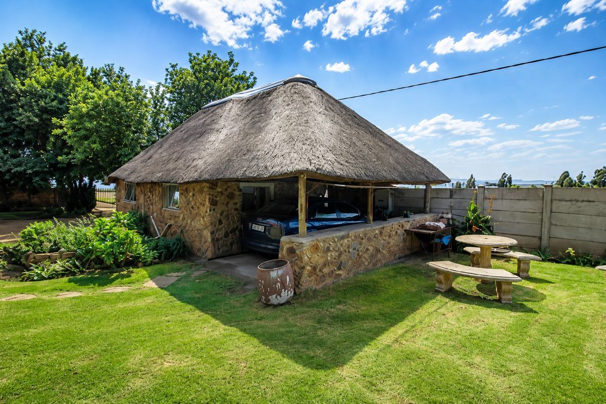 A rustic farm-style building featuring traditional stone cladding and a thatched roof, with an integrated covered patio area overlooking a well-maintained garden.