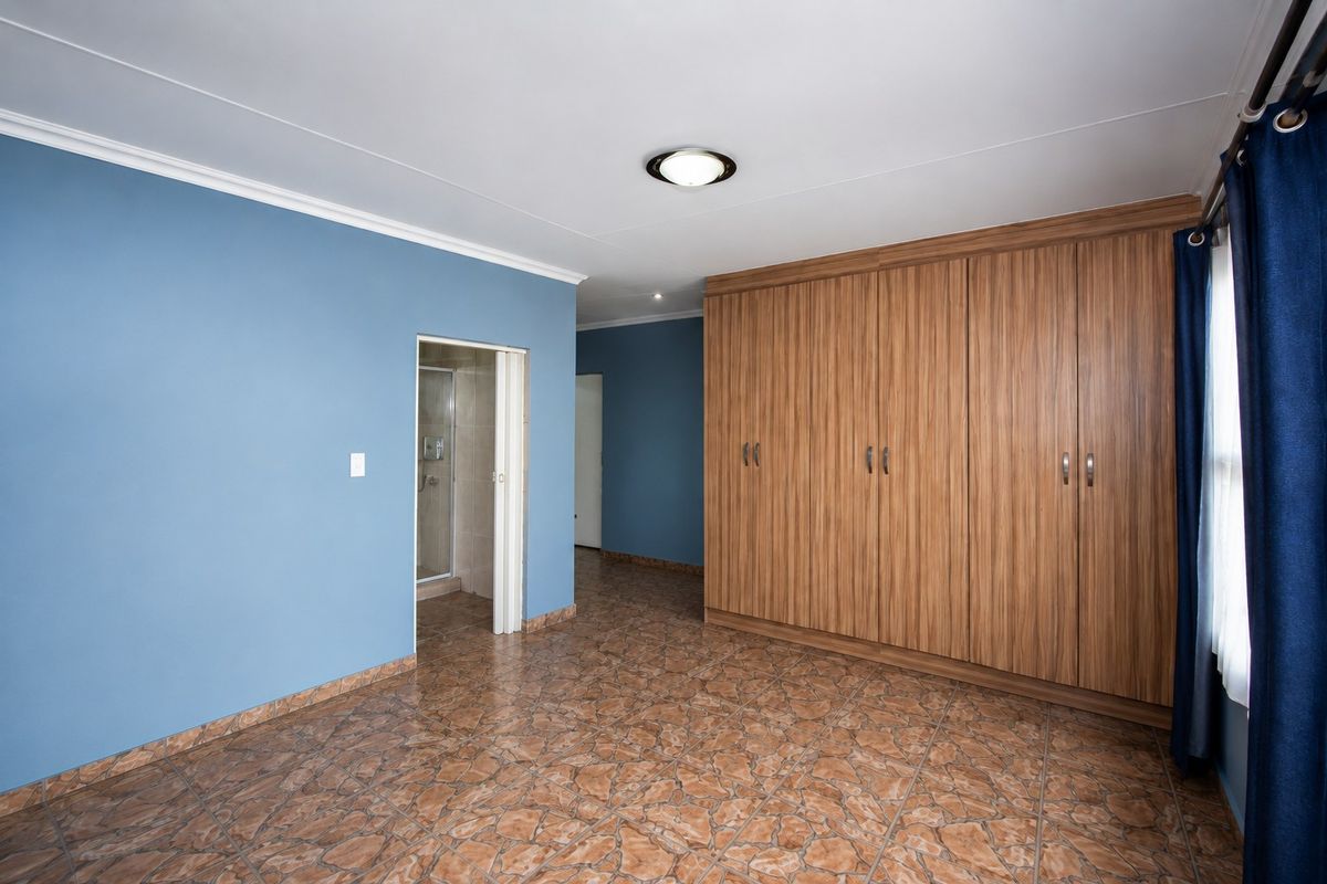 Spacious bedroom featuring built-in wooden cupboards, tiled flooring, and direct access to an en-suite bathroom.