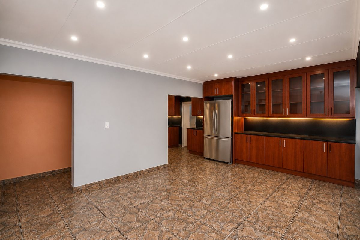 A spacious, well-lit kitchen area featuring extensive dark wood cabinetry, stone countertops, and durable tiled flooring, offering a clean and functional layout.