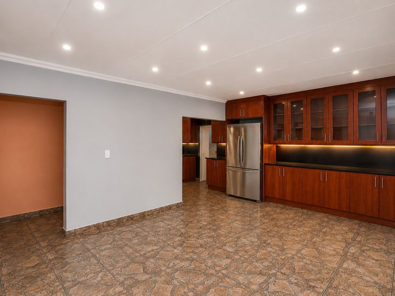 A spacious, well-lit kitchen area featuring extensive dark wood cabinetry, stone countertops, and durable tiled flooring, offering a clean and functional layout.