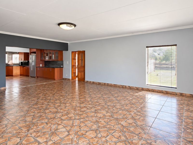 Spacious open-plan living area featuring tiled flooring, neutral walls, and an adjoining kitchen with built-in cabinetry and direct access to the rest of the home.
