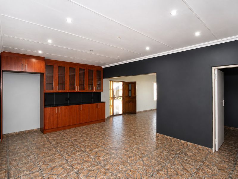 Spacious open-plan living area featuring tiled flooring, recessed lighting, and built-in wooden cabinetry with dark stone countertops.