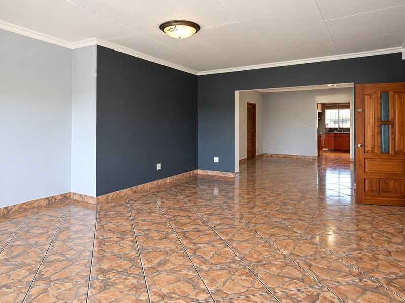 Spacious open-plan living area featuring tiled flooring, neutral and accent wall tones, and a solid wooden door leading to adjacent rooms.