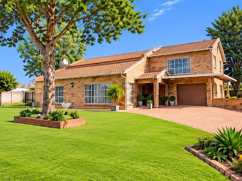 A well-maintained double-story brick farmhouse featuring a paved driveway, integrated garage, and expansive manicured lawn under a clear blue sky.