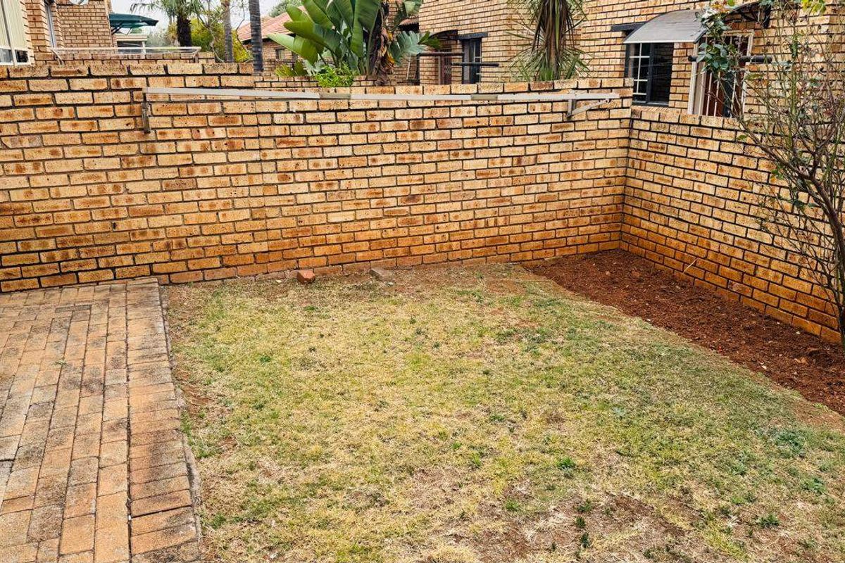 A private rear courtyard featuring a brick boundary wall, a paved patio section, and a small garden area with a wall-mounted washing line.