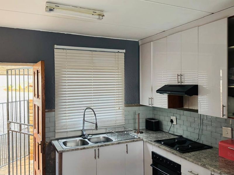 Functional kitchen featuring white cabinetry, subway tile backsplash, granite-look countertops, and integrated appliances, with direct access to the exterior.