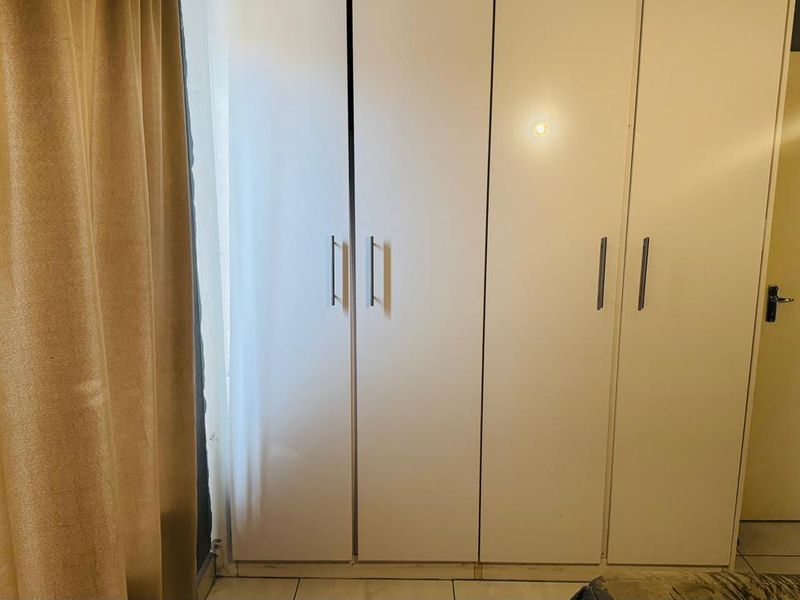 A bedroom featuring white built-in cupboards and tiled flooring, providing functional storage space.