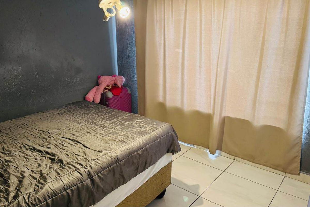 A bedroom featuring tiled flooring and a dark accent wall, providing a functional space with neutral window treatments.