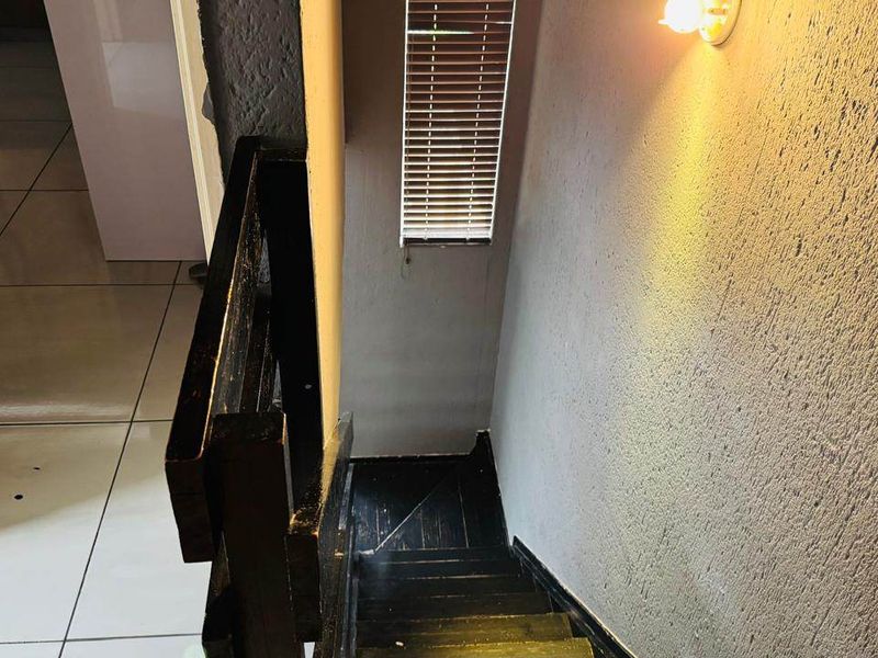 A staircase area featuring a wooden balustrade, textured wall finishes, and tiled flooring, leading to the lower level of the townhouse.