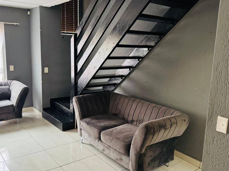 Living area featuring a dark painted staircase, tiled flooring, and neutral grey walls.