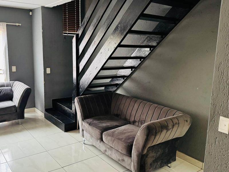 Living room area featuring a prominent black staircase, tiled flooring, and neutral grey walls, providing a functional space with modern design elements.