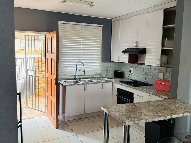 Compact kitchen featuring white cabinetry, stone-look countertops, built-in oven and hob, tiled backsplash, and direct access to an exterior security gate.