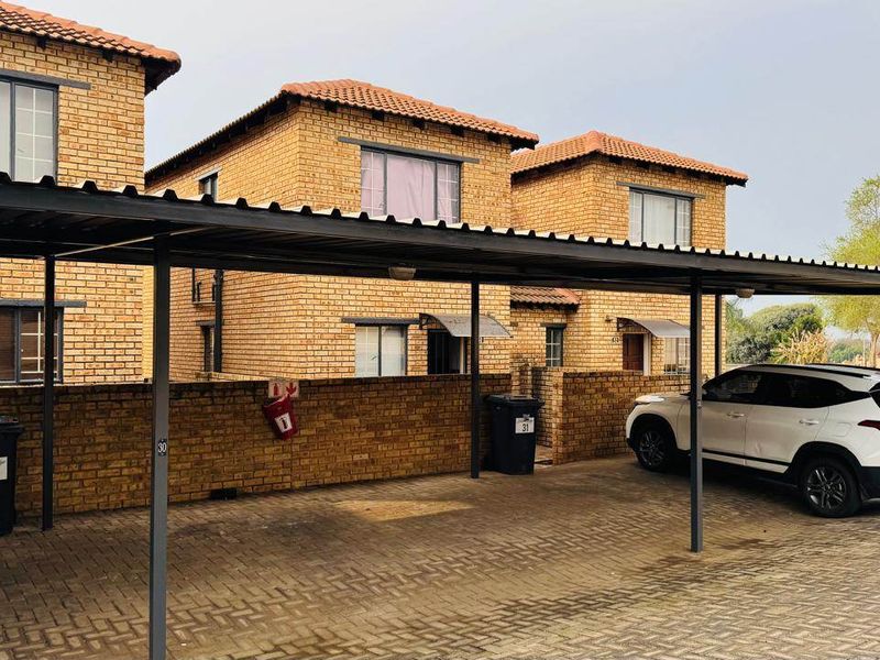 Front view of a townhouse complex featuring face-brick construction, a covered carport, and paved driveway area.