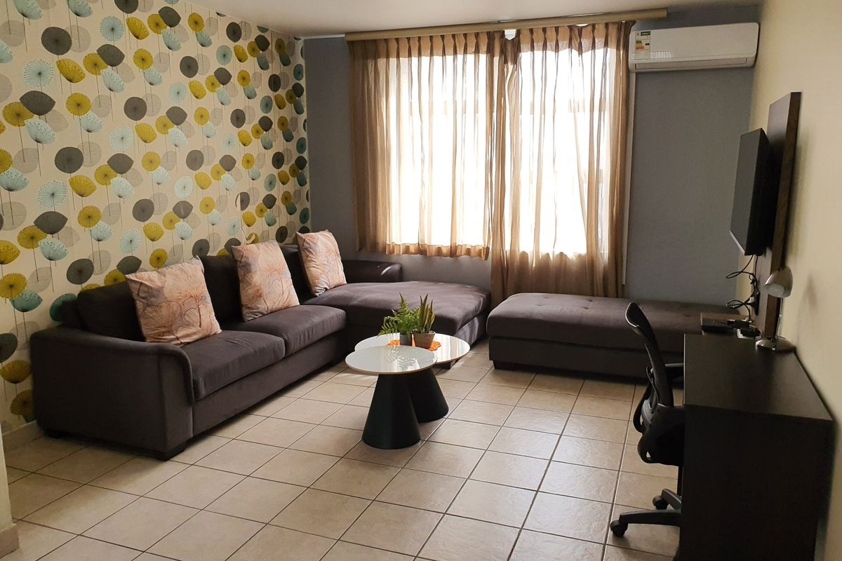 A living room featuring tiled flooring, a wall-mounted split-system air conditioner, and a decorative feature wall.