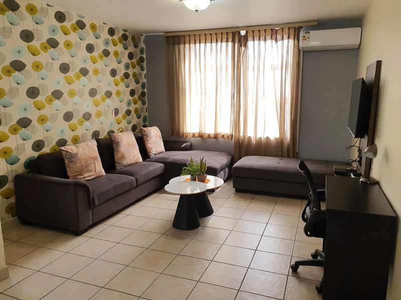 A living room featuring tiled flooring, a wall-mounted split-system air conditioner, and a decorative feature wall.