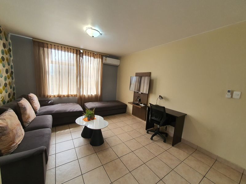 A functional living room featuring tiled flooring, a wall-mounted air conditioning unit, and a dedicated television mounting panel.