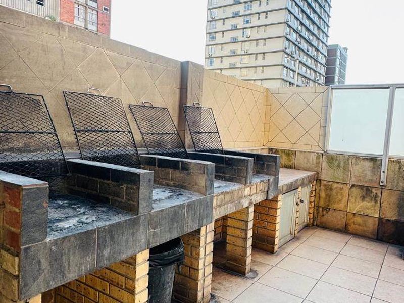 Outdoor balcony area featuring multiple built-in braai stations with tiled flooring and masonry walls, offering an urban view.