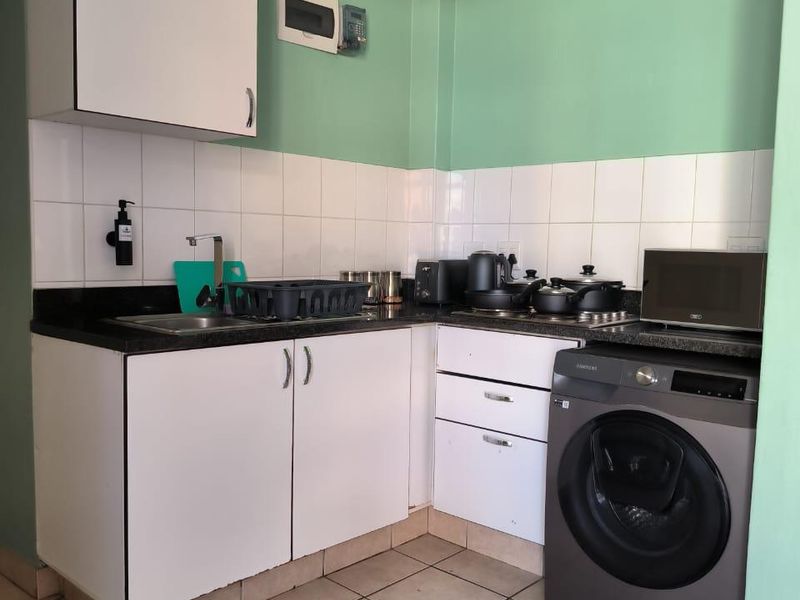 Compact kitchen featuring white cabinetry, dark countertops, tiled backsplash, and integrated laundry facilities, offering a functional layout for an apartment setting.