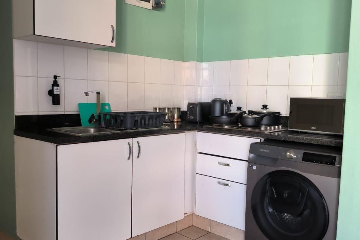 Compact kitchen featuring white cabinetry, dark countertops, tiled backsplash, and integrated laundry facilities, offering a functional layout for an apartment setting.