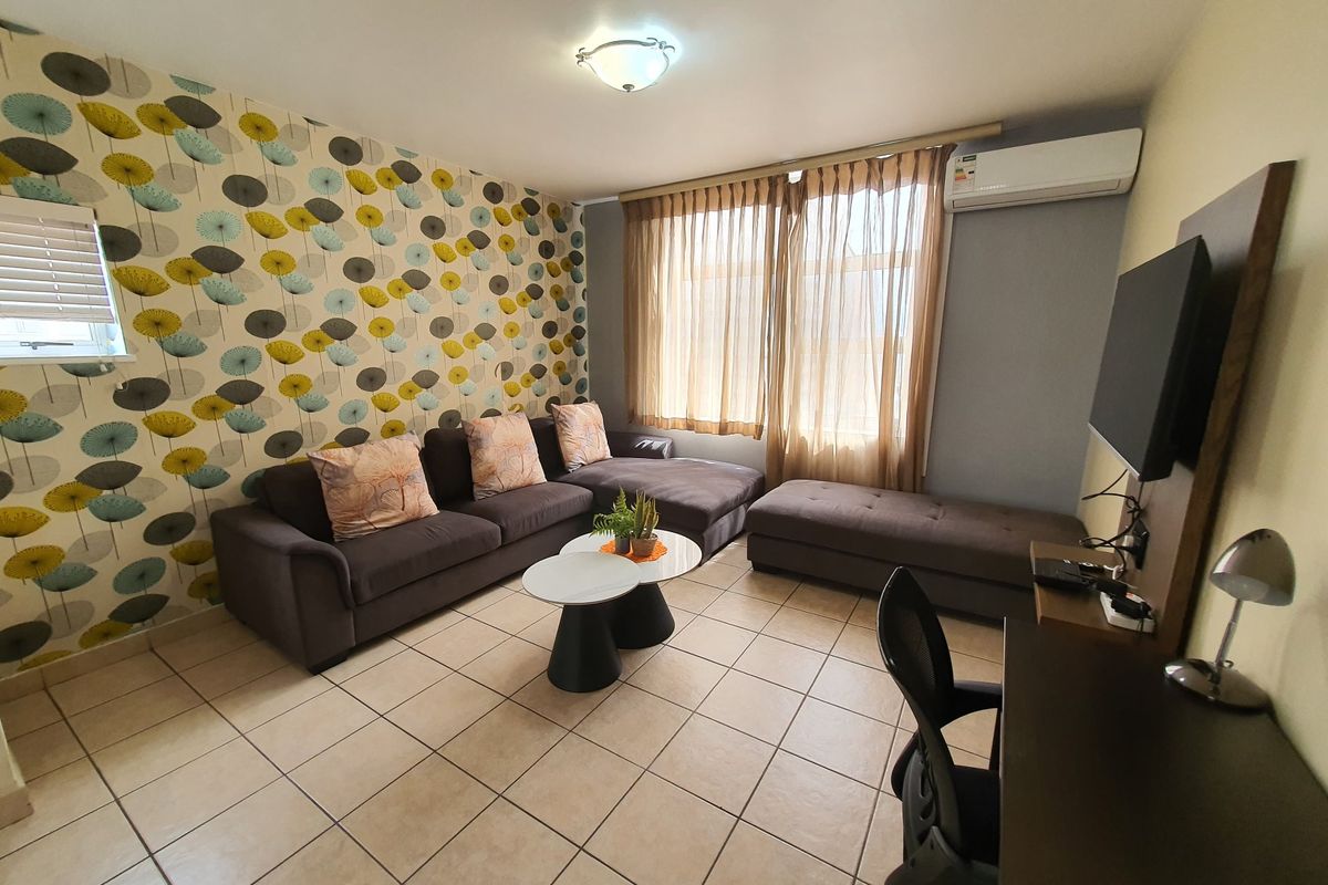 A living room featuring ceramic floor tiles, a wall-mounted split-system air conditioner, and a decorative feature wall.
