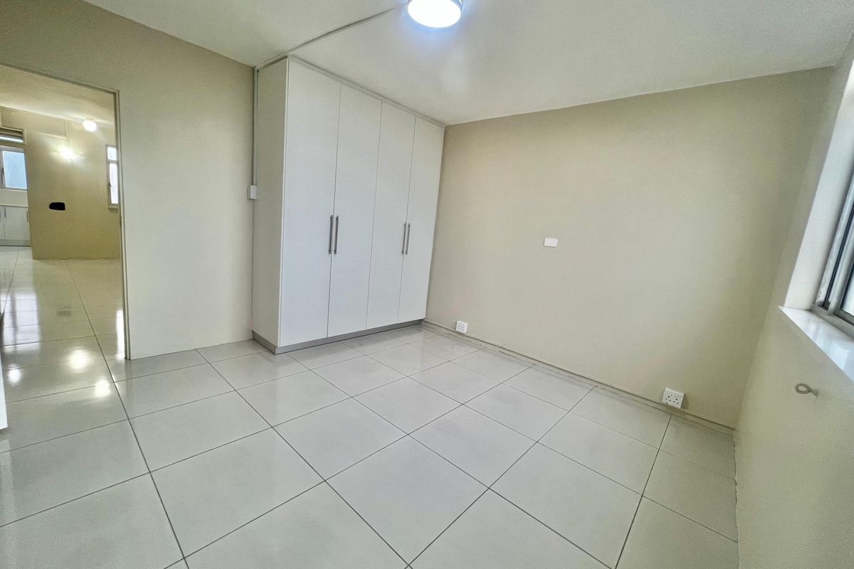A bright, empty bedroom featuring neutral tiled flooring and a large built-in wardrobe with white cabinetry.