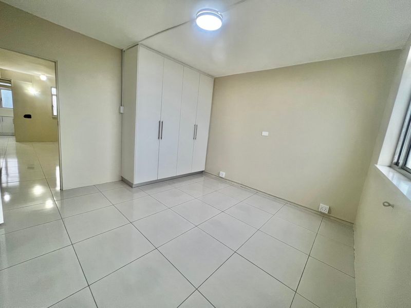 A bright, empty bedroom featuring neutral tiled flooring and a large built-in wardrobe with white cabinetry.