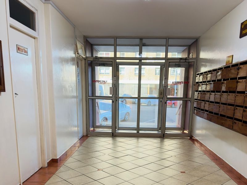 A functional apartment building entrance lobby featuring tiled flooring, a bank of mailboxes, and secure aluminium-framed glass doors leading to the exterior.