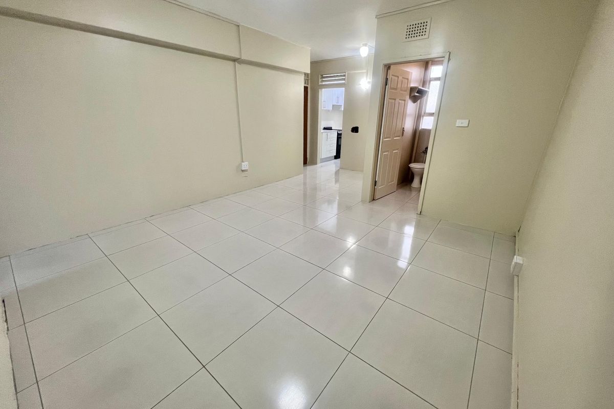 A bright, empty living area featuring neutral tiled flooring and access to adjacent rooms, providing a clean canvas for interior design.