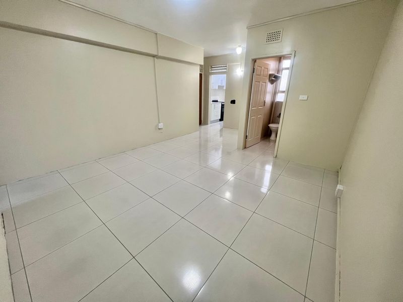 A bright, empty living area featuring neutral tiled flooring and access to adjacent rooms, providing a clean canvas for interior design.