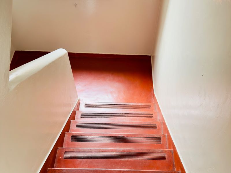 A functional interior staircase featuring painted concrete steps with integrated tread grips and a solid balustrade, leading to a landing with a small window.