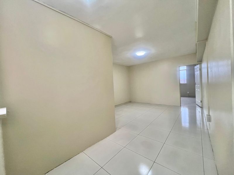 An empty, open-plan living area featuring neutral walls and clean tiled flooring, providing a versatile space ready for personalization.