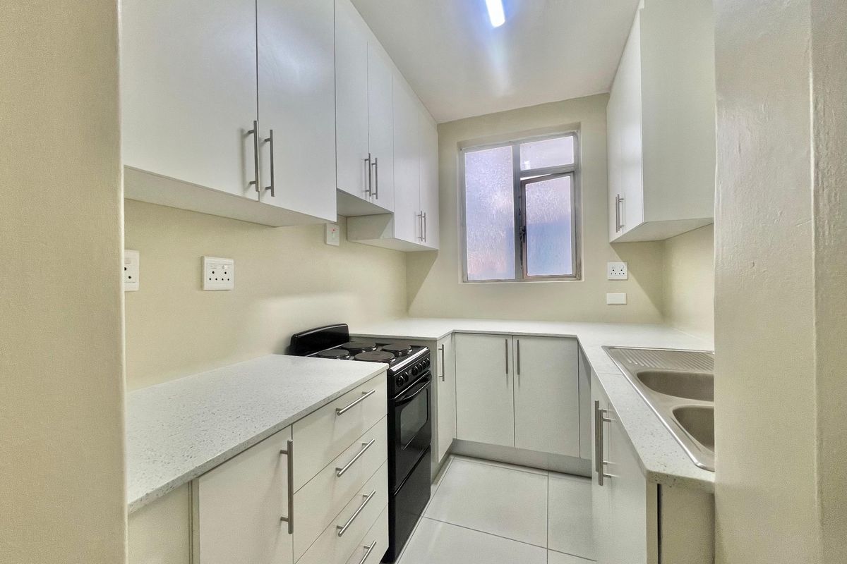 A clean, modern kitchen featuring white cabinetry, stone-look countertops, a stainless steel double sink, and a freestanding electric stove with tiled flooring.