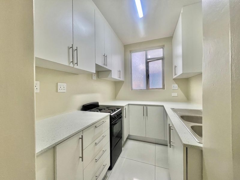 A clean, modern kitchen featuring white cabinetry, stone-look countertops, a stainless steel double sink, and a freestanding electric stove with tiled flooring.