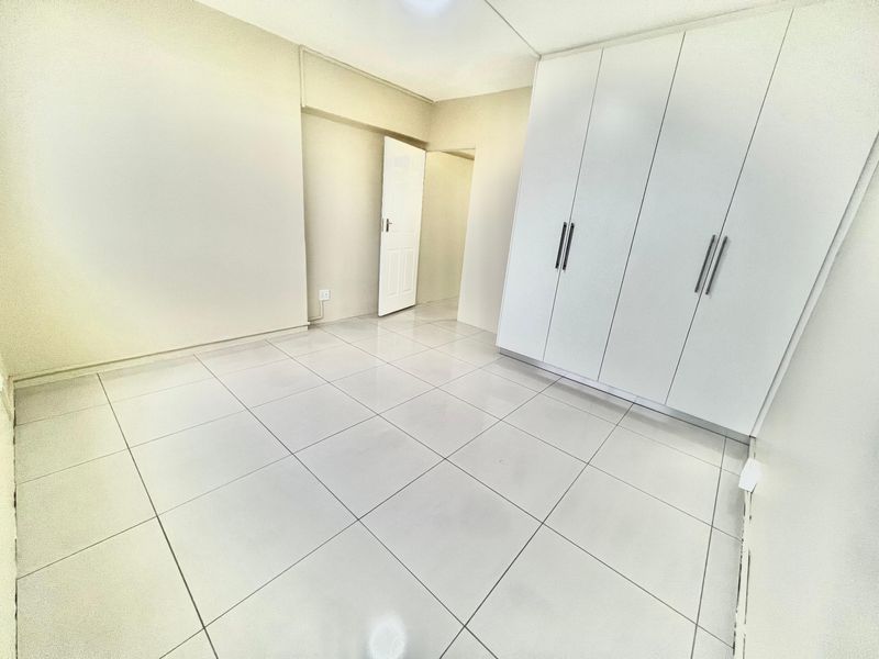 A bright, empty bedroom featuring neutral tiled flooring and modern white built-in cupboards, offering a clean and versatile living space.