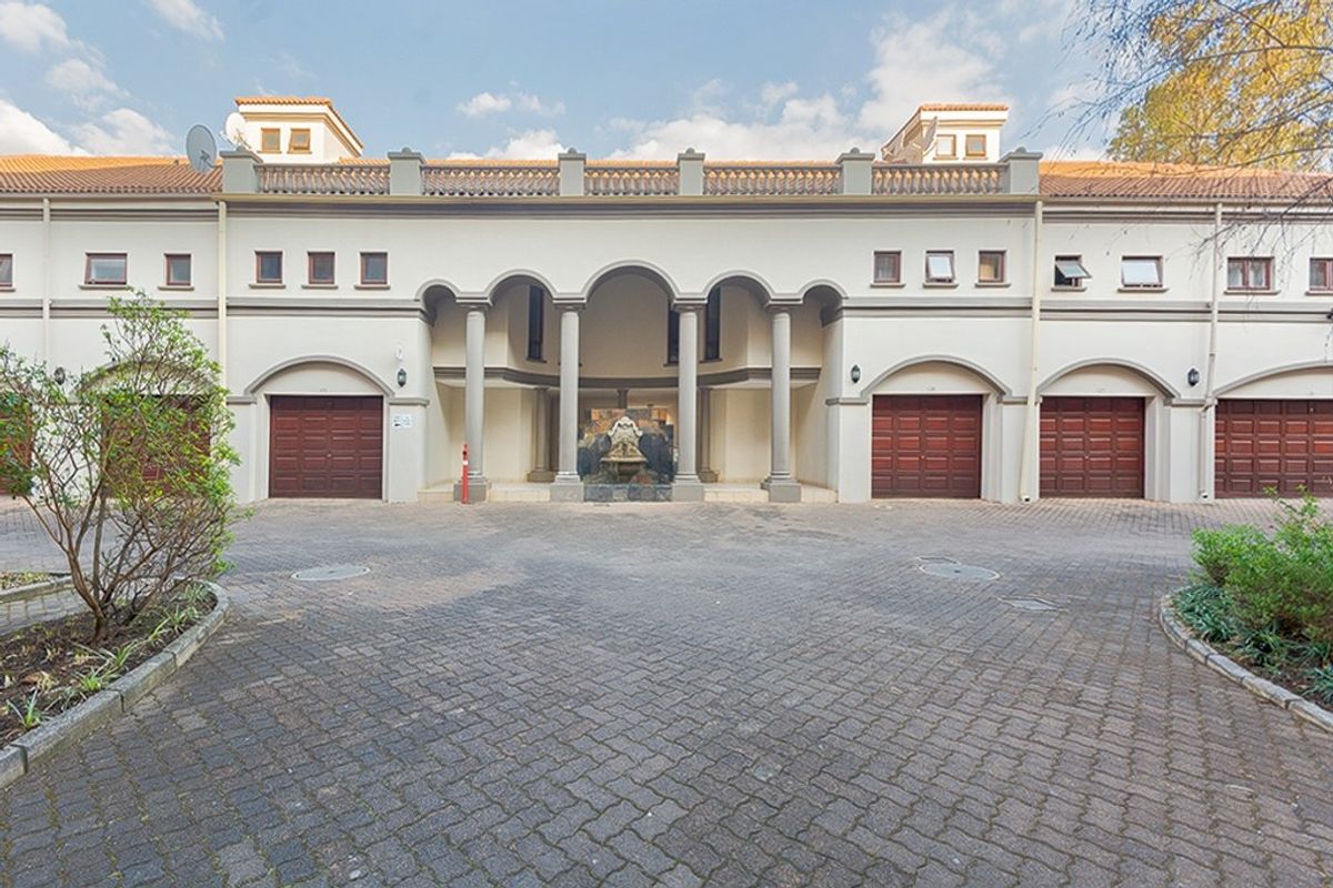 Front elevation of an apartment complex featuring a paved driveway, multiple garage doors, and a central arched entrance with a decorative water feature.