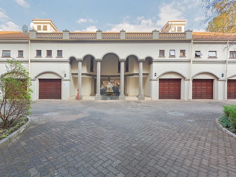 Front elevation of an apartment complex featuring a paved driveway, multiple garage doors, and a central arched entrance with a decorative water feature.