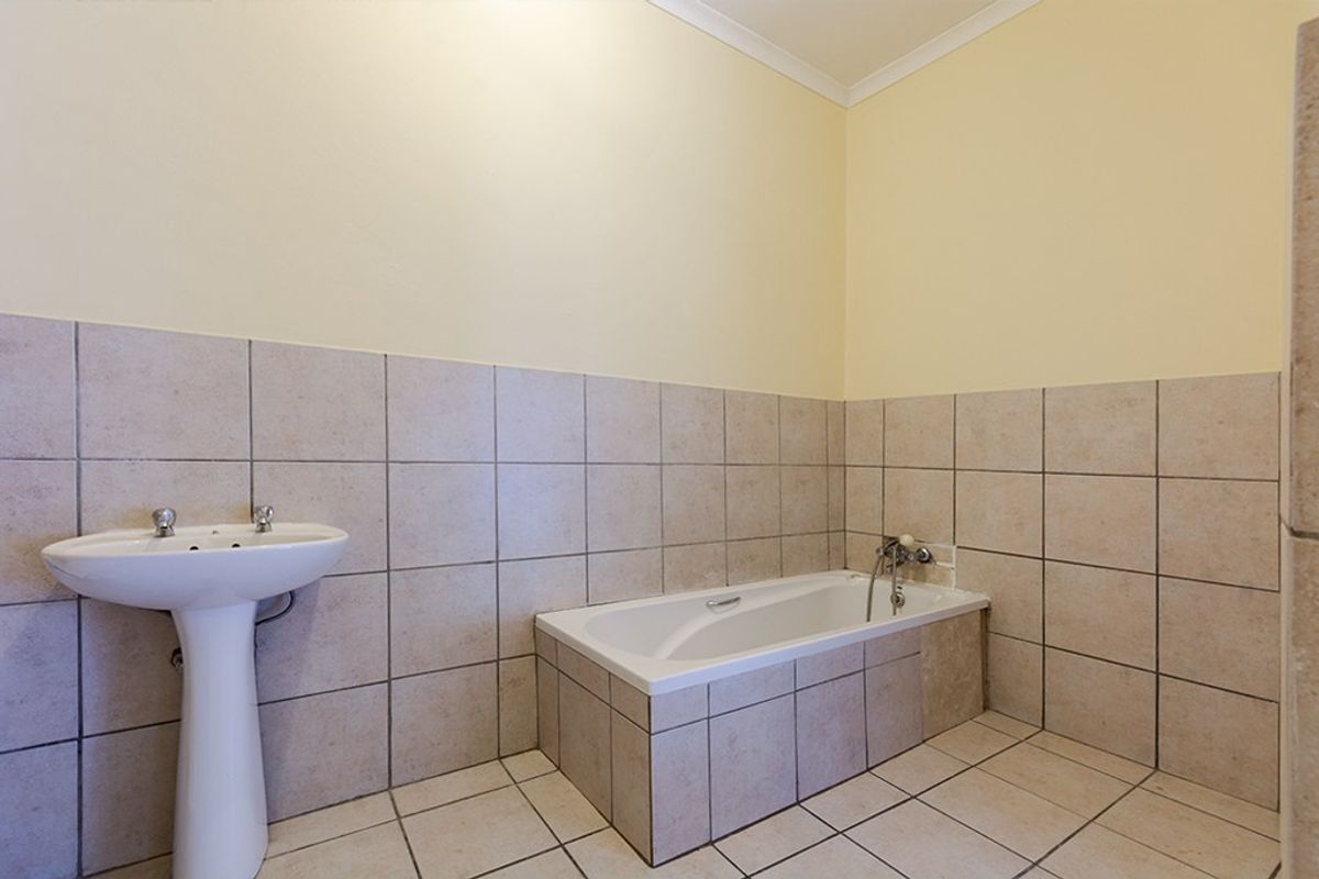 A functional bathroom featuring a built-in bathtub with tiled surround and a classic pedestal basin, finished with neutral ceramic wall and floor tiles.