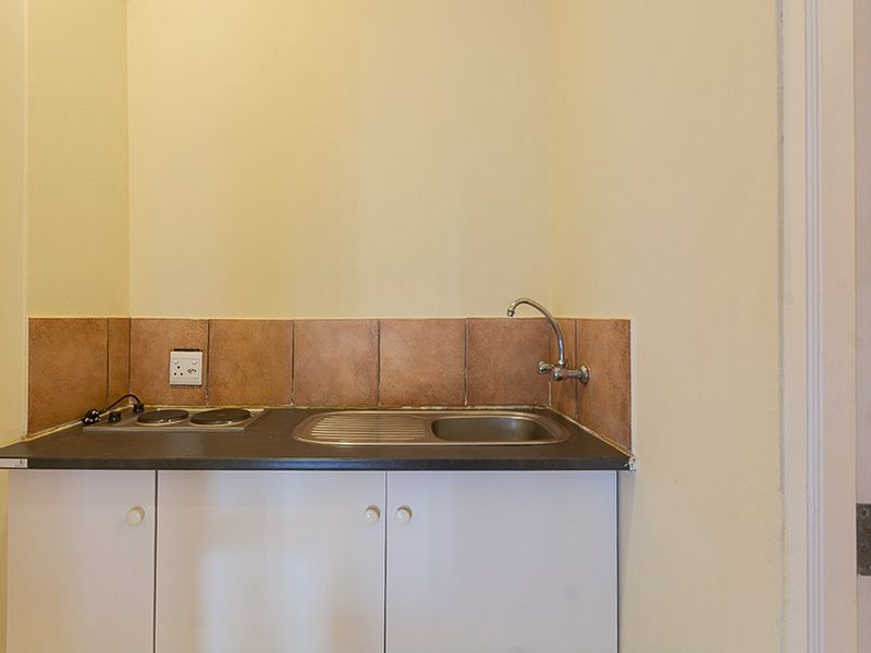 A compact kitchenette featuring built-in white cabinetry, a dark laminate countertop, a stainless steel sink, and a two-plate electric hob with tiled splashback.