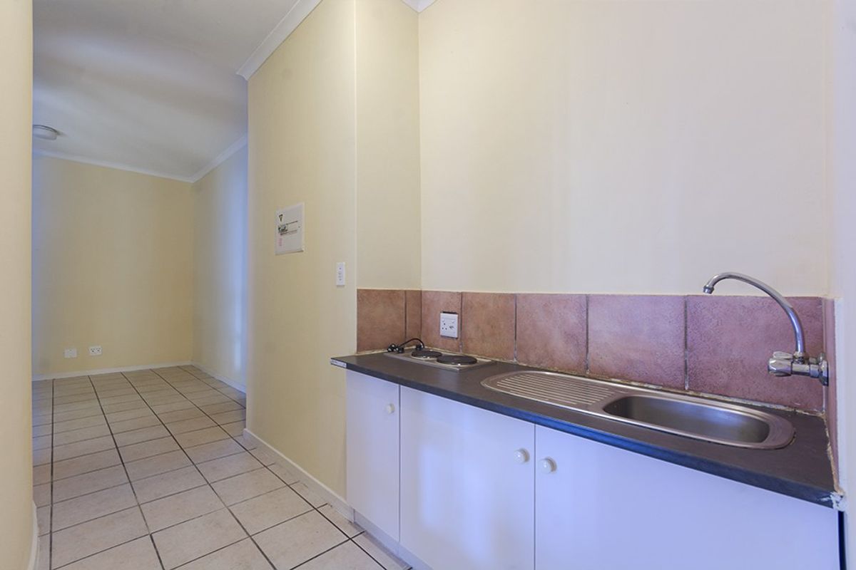 A compact kitchenette featuring a stainless steel sink, built-in hob, and tiled backsplash, leading into an open-plan living area with tiled flooring.