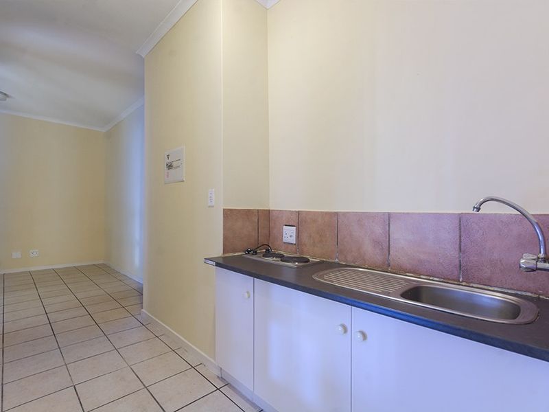 A compact kitchenette featuring a stainless steel sink, built-in hob, and tiled backsplash, leading into an open-plan living area with tiled flooring.