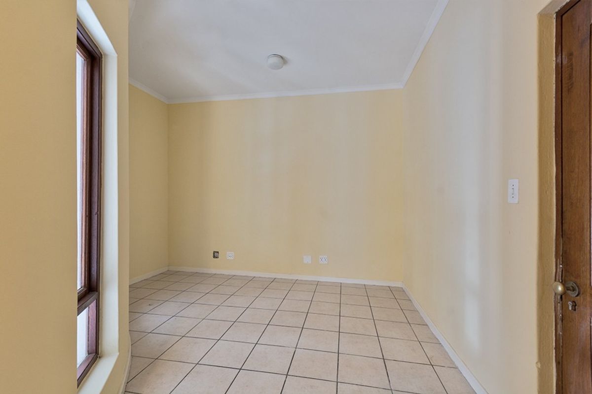 An empty bedroom featuring neutral wall paint, tiled flooring, a wooden door, and a window, providing a blank canvas for personalization.
