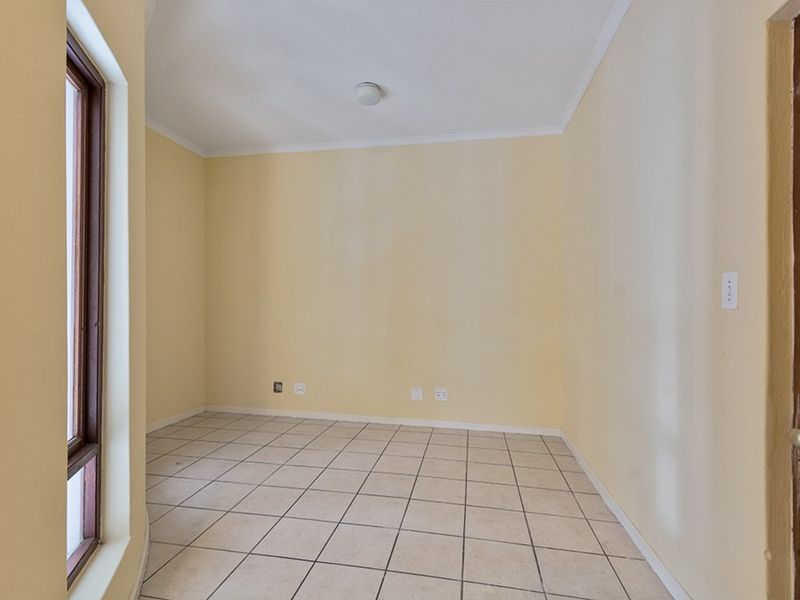 An empty bedroom featuring neutral wall paint, tiled flooring, a wooden door, and a window, providing a blank canvas for personalization.